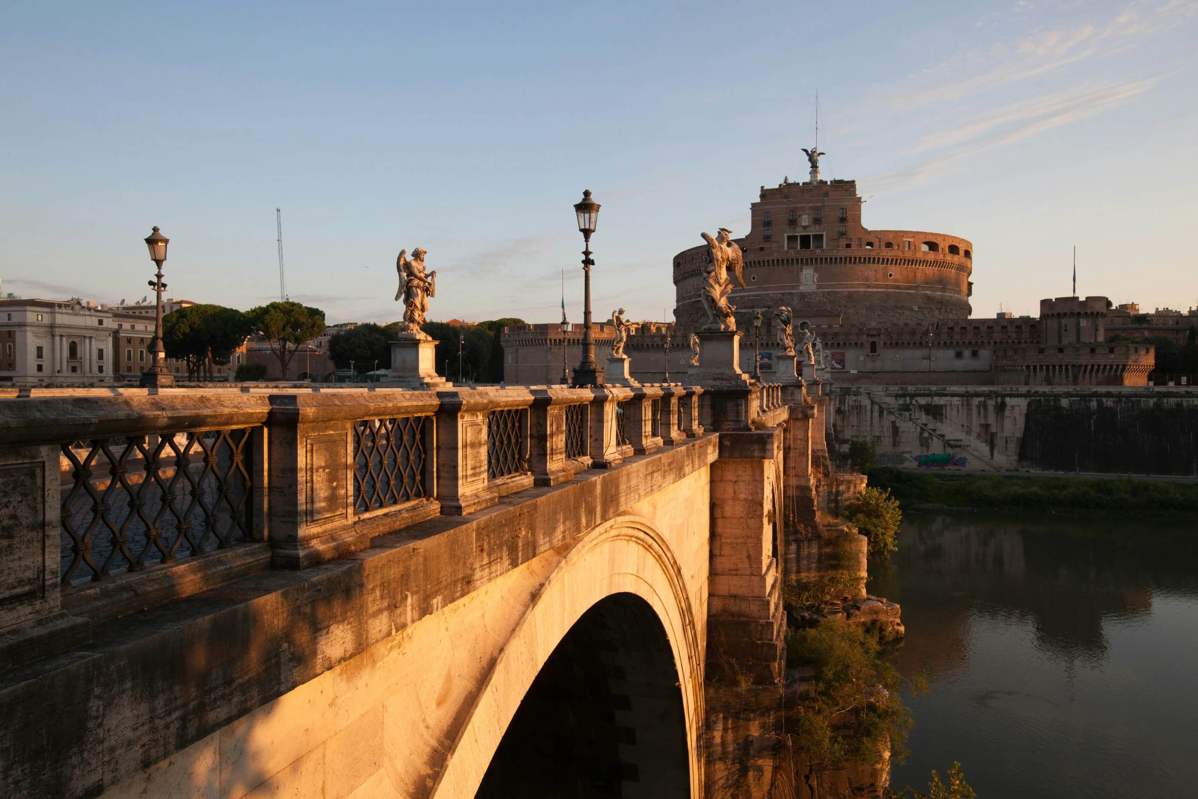 the sun sets on the bridge over water and a building