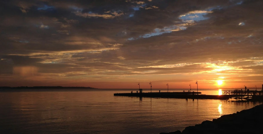 a sunrise is shining behind a dock in the water