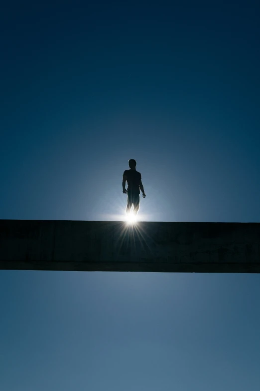a man walking down a bridge with the sun shining behind him