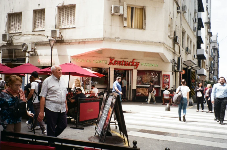 some people people buildings red umbrellas and tables