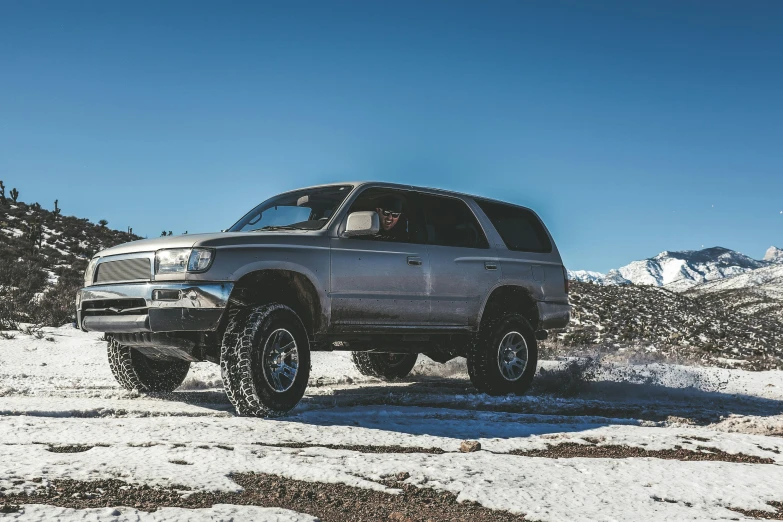 the pickup truck is driving through snow on top of a mountain