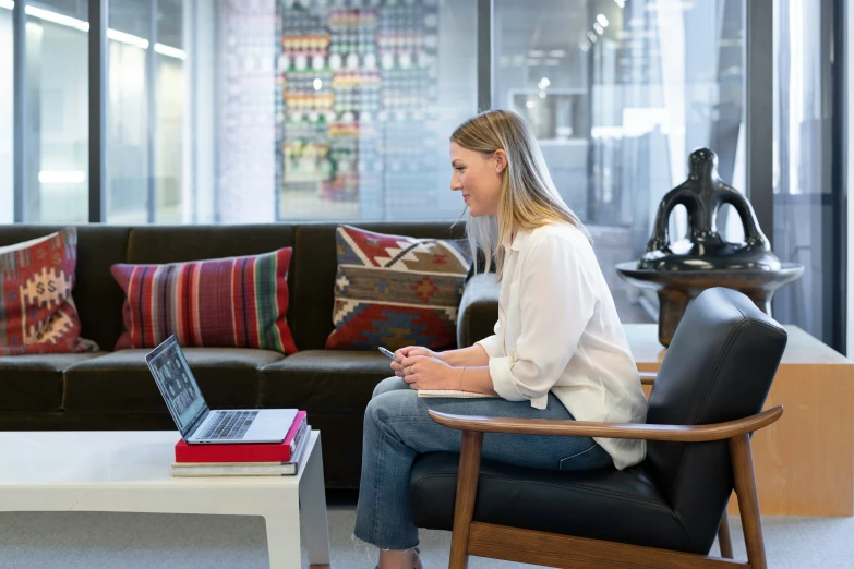 a woman sitting on a chair next to a brown couch in front of a laptop