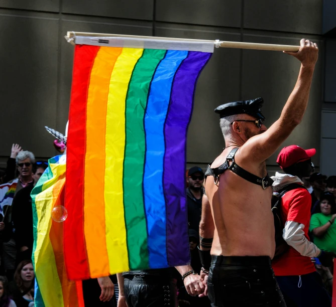a man holding a large rainbow flag with gay pride written on it