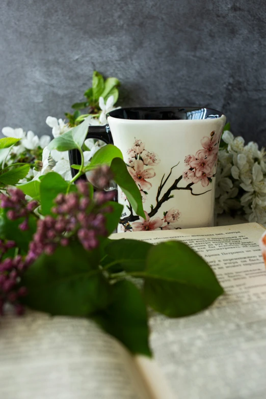 a coffee cup sitting next to flowers in an open book
