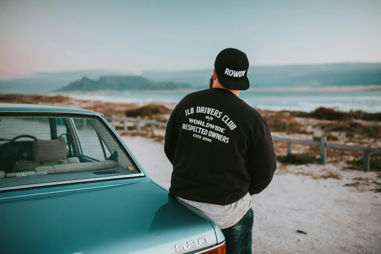 a person leaning on the back of a car in front of a beach