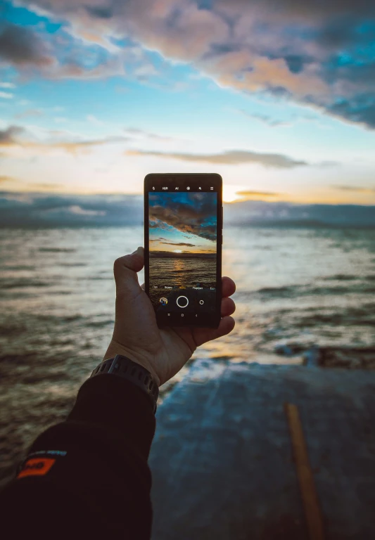 a person taking a picture on their cell phone in front of the ocean