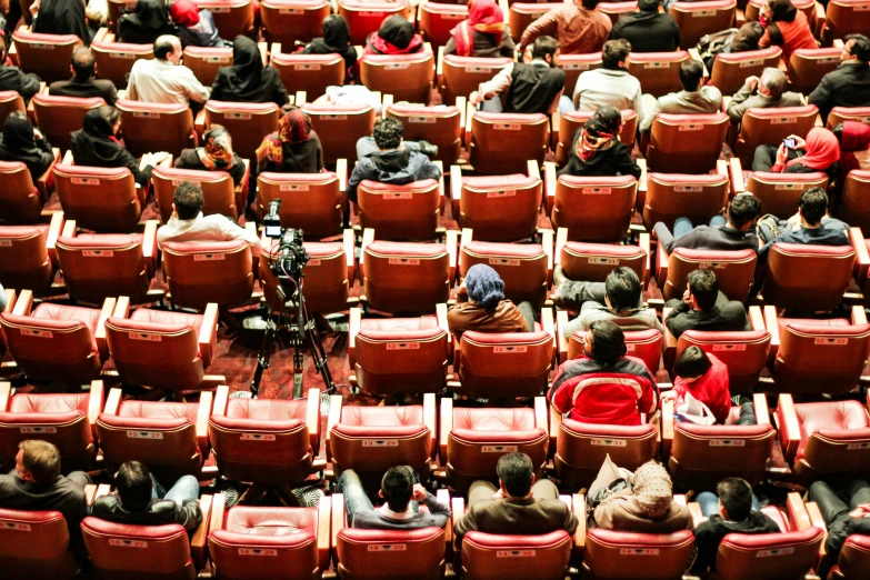 large group of people sitting in rows with red seats