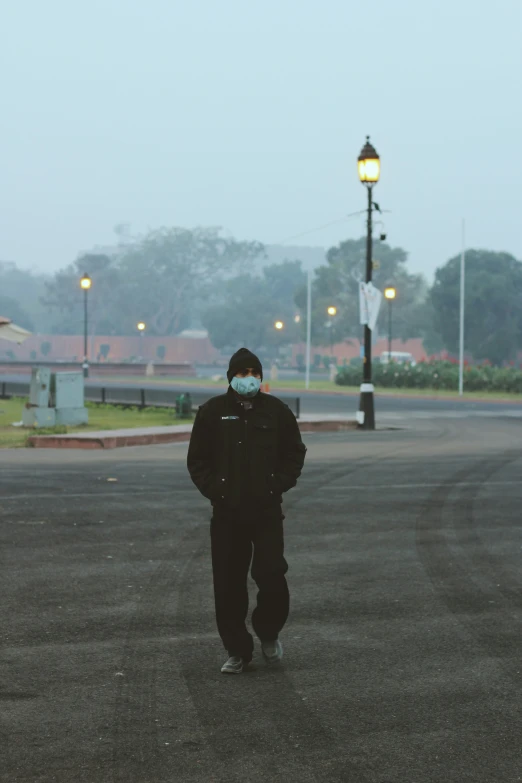 man wearing face mask walking down a paved street at twilight