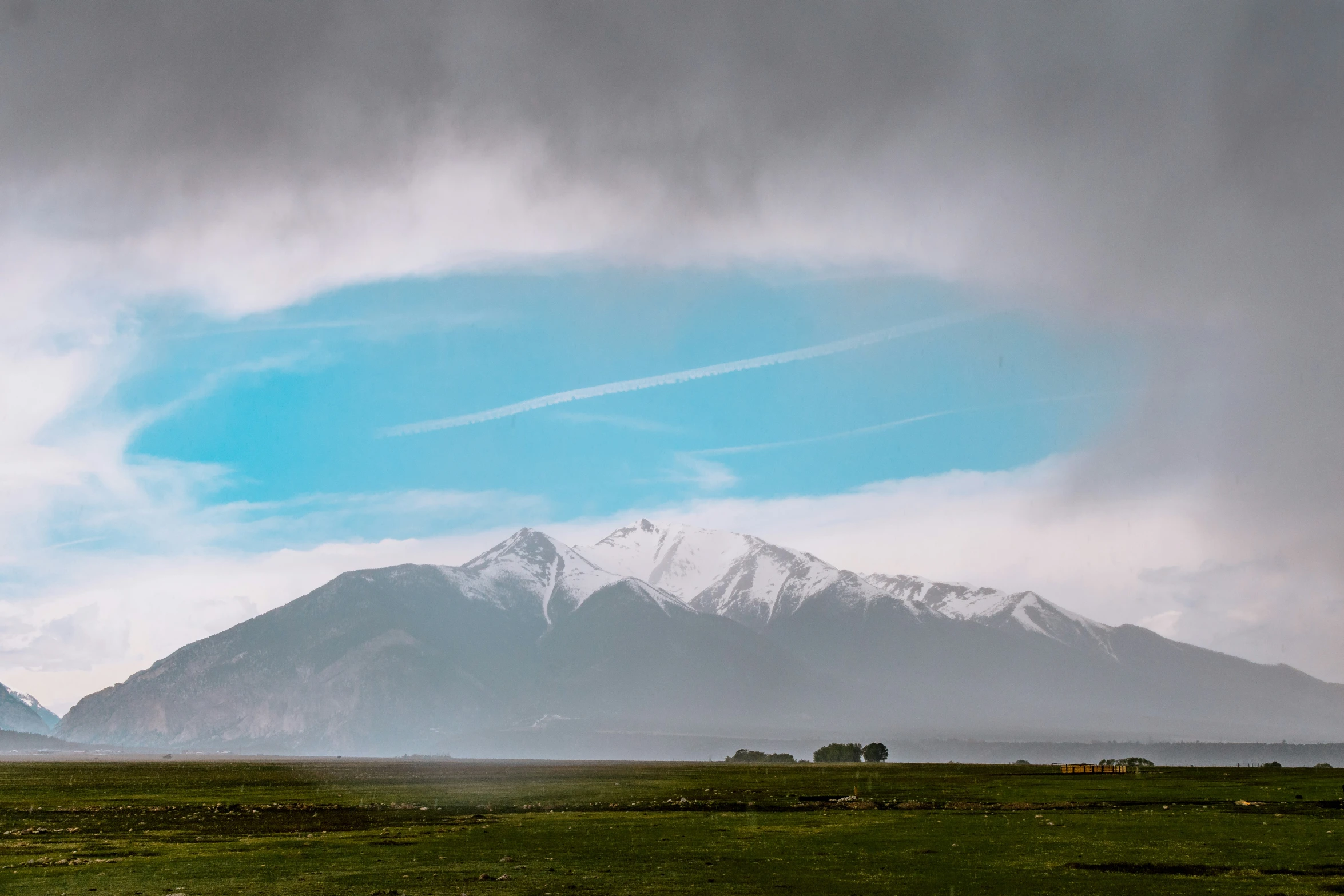 a field with two buildings and snowy mountains in the distance