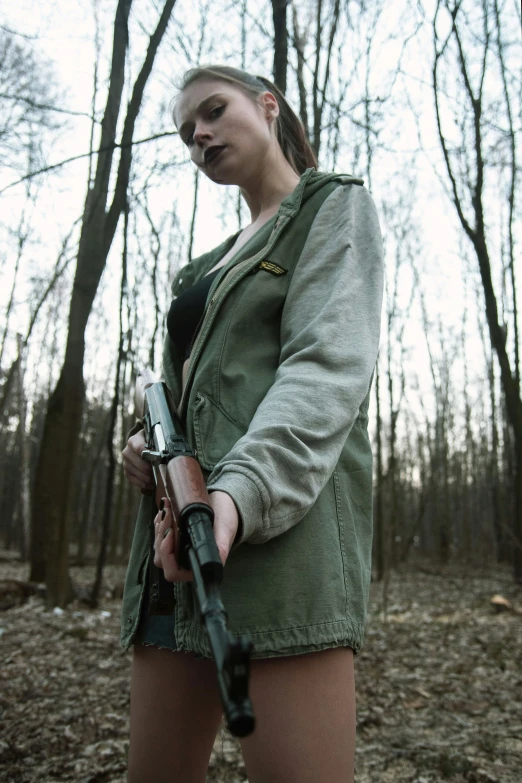 a young woman holding a gun while standing in a forest