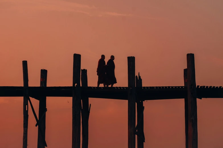 a couple walking along a pier while the sun is setting