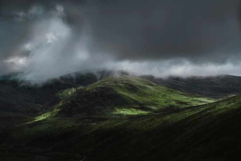 the clouds are rolling over the tops of hills