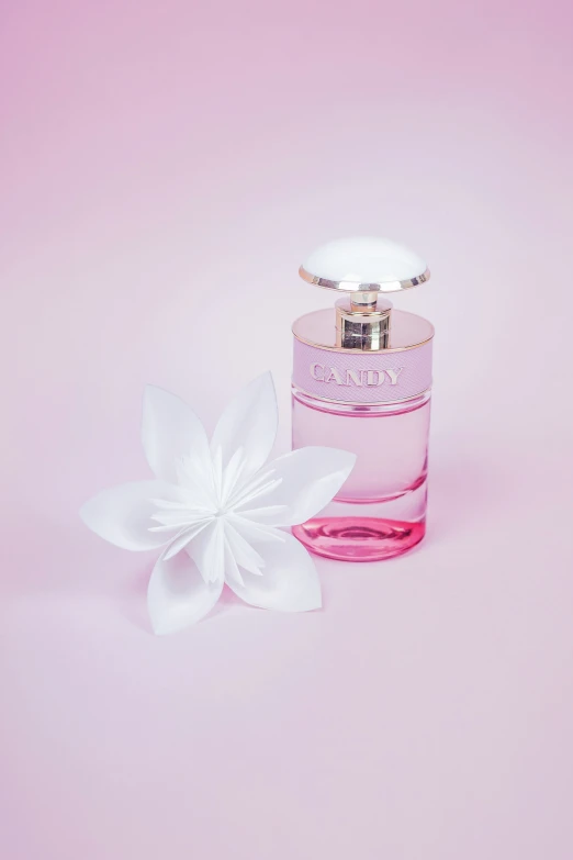 an open pink perfume bottle sitting next to a white flower