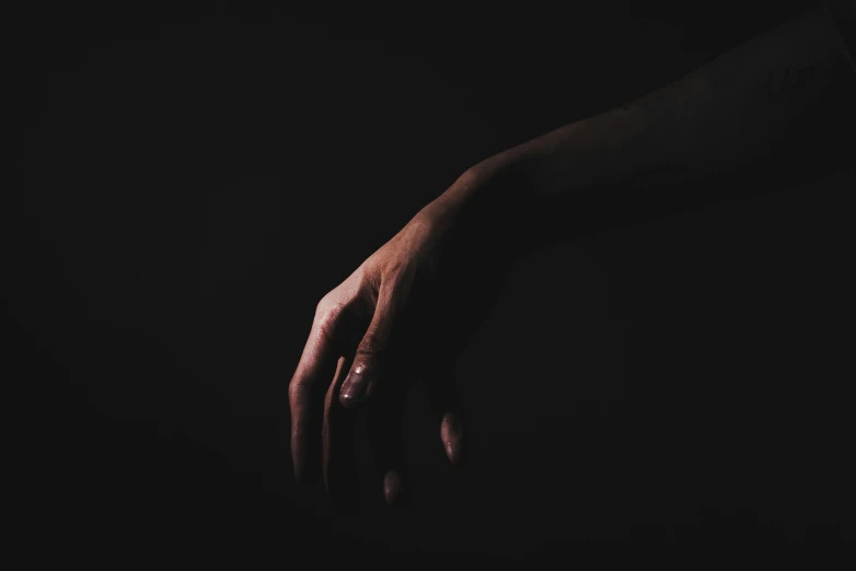 a dark silhouette of two hands with light and shadow on one hand, which appears to be reaching for soing