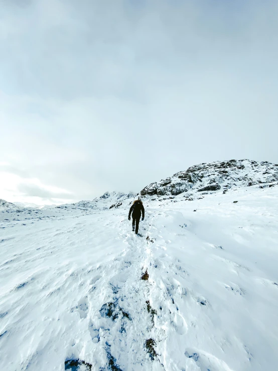 a man walking uphill on a snowy mountain