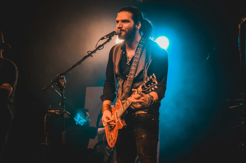 a man in a black suit playing guitar and singing into a microphone