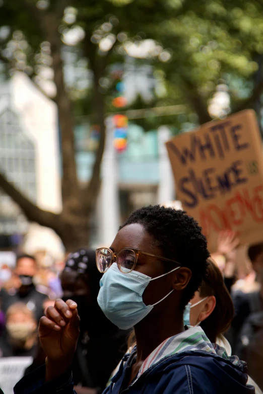 a woman in black jacket holding sign and wearing a mask