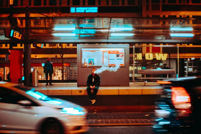 a man sitting outside of a building while traffic passes by