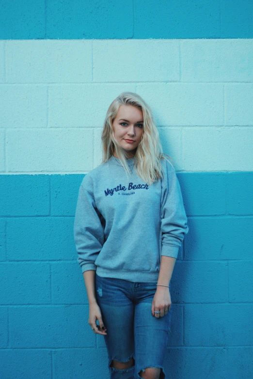 young woman standing against a blue wall wearing ripped jeans