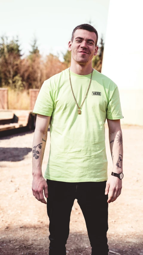 a man with a cross on his left hand and a tattoo on his right hand standing in front of a white building