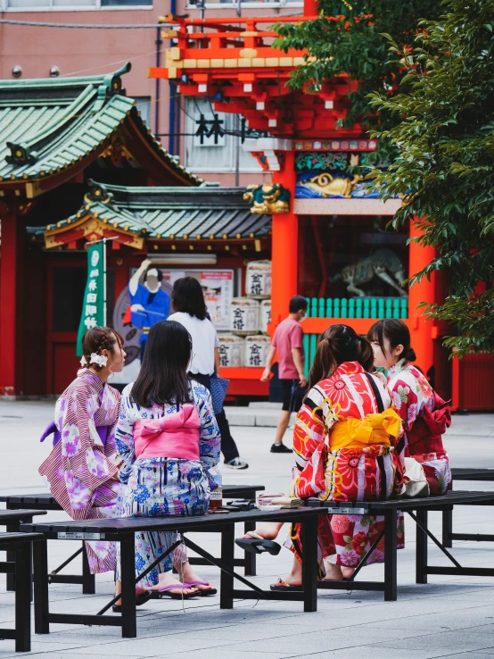 a group of four women wearing kimonos sitting on benches