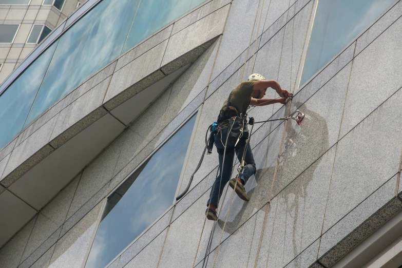 a man climbing a building, using a safety harness and rope to climb up the side