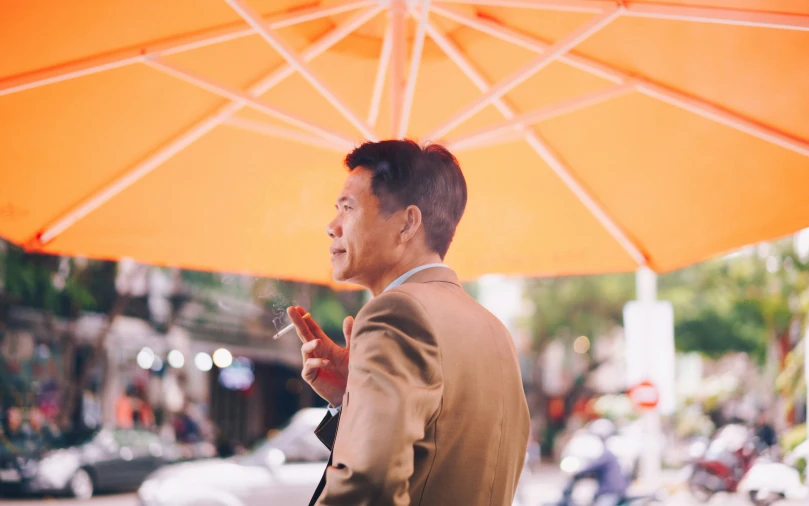 a man standing under an umbrella holding a cigarette