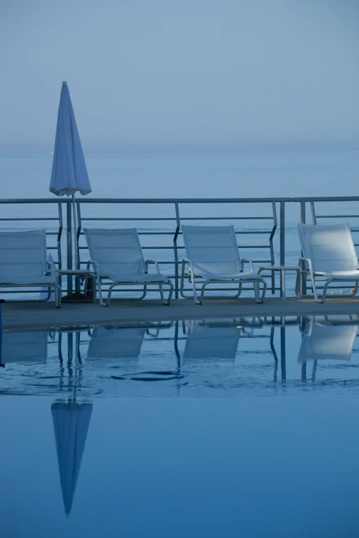 a row of chairs and an umbrella sitting on a pier next to a swimming pool