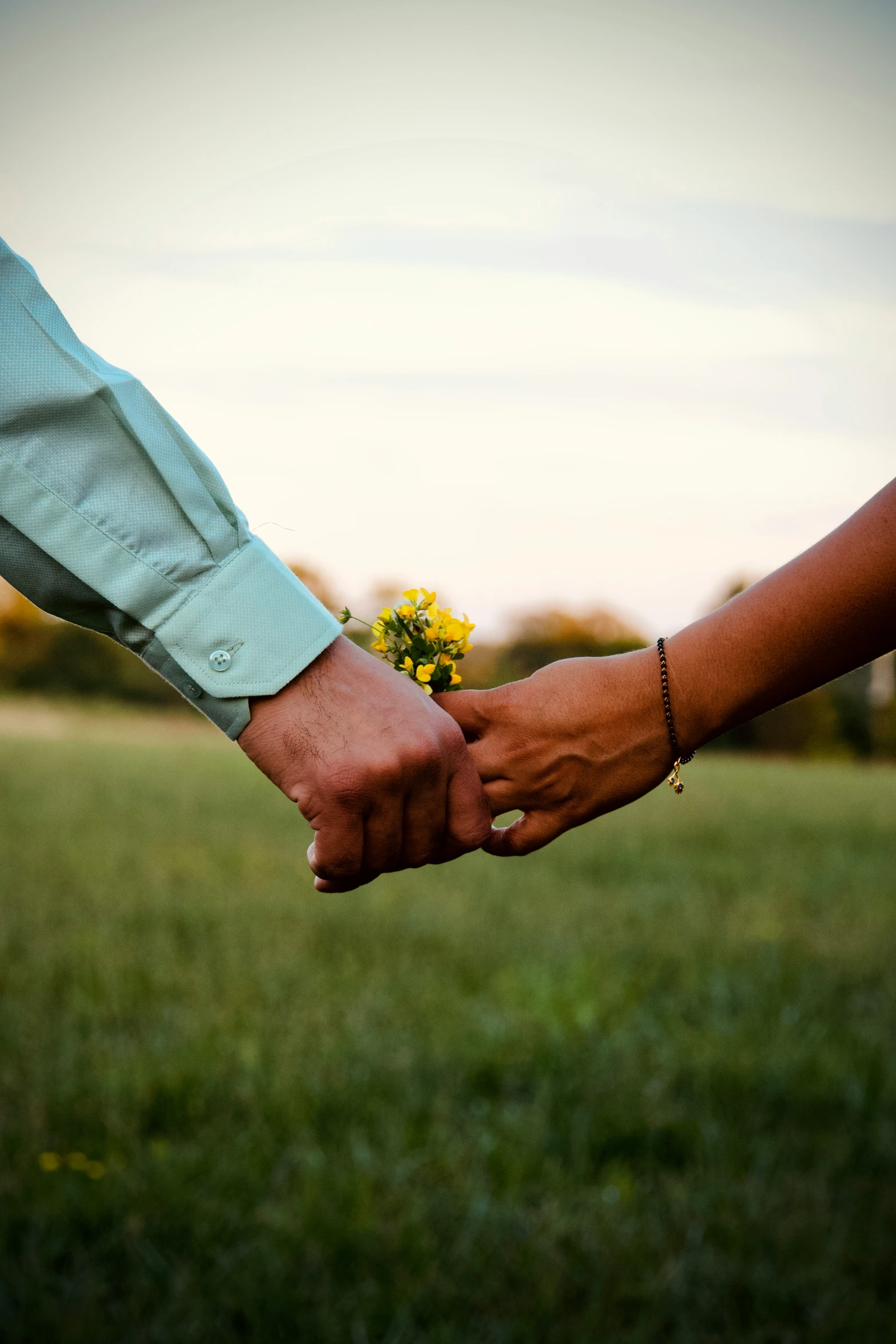 two people are holding hands with a yellow flower