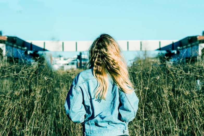 a woman standing in tall grass with a bridge in the background