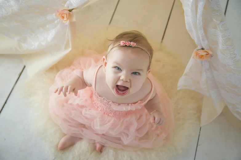 baby wearing a dress and sitting in the center of a floor