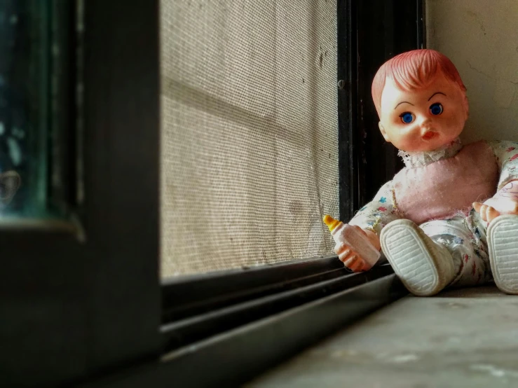 a close up of a small doll sitting on a window sill