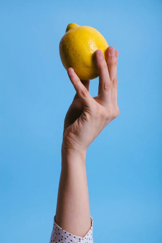 a person holding up an orange with a blue background