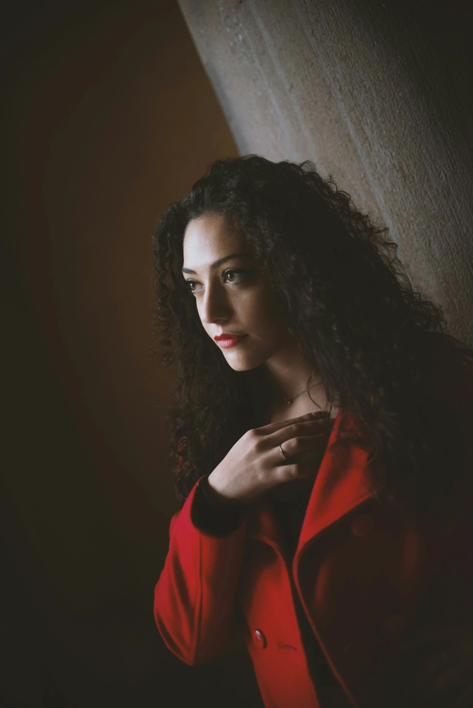 the woman in a red coat poses by a wall