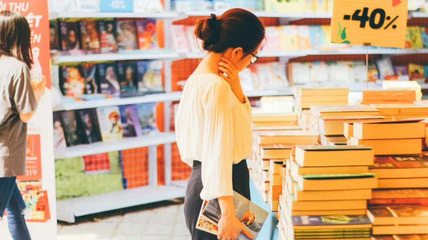 a girl in glasses walking past a books shelf while holding a purse