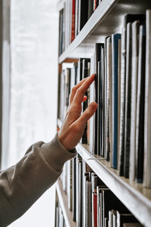 a person's hand reaching for books on a book shelf