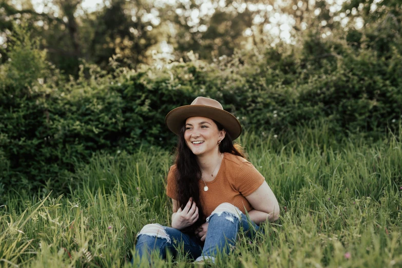 a woman is sitting in the grass with a brown hat on