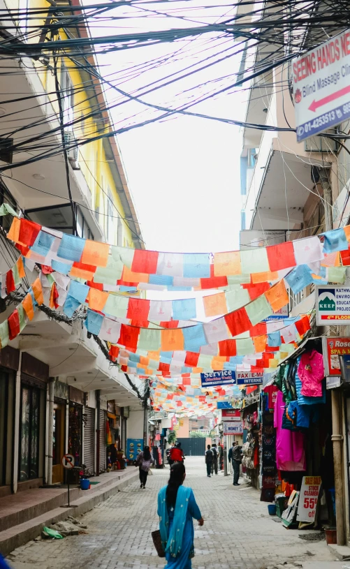 a woman in a blue dress walks under many colored flags