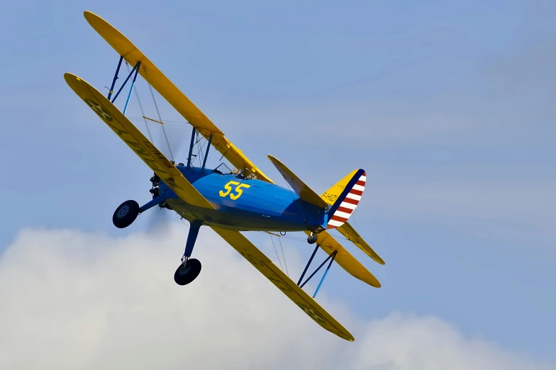 a blue and yellow biplane flying over a cloud