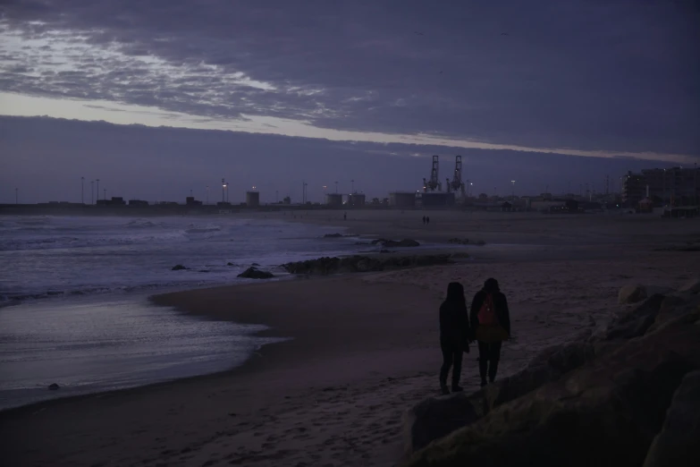 two people walking down the beach at dusk