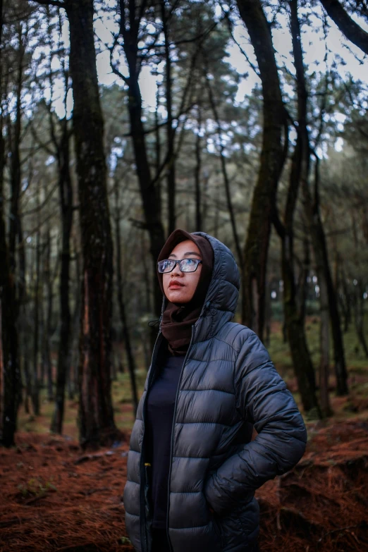 a woman with glasses standing in front of a wooded area