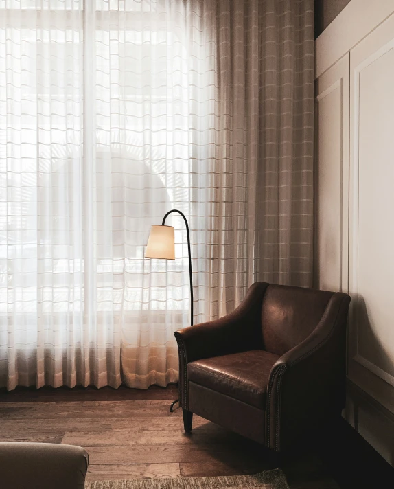 a bedroom with a white sheer curtain and brown chair