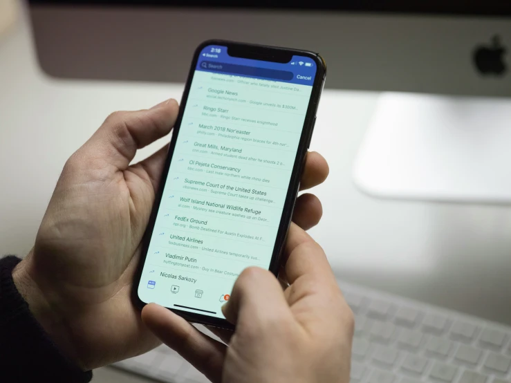 a person is holding an iphone while sitting at a desk