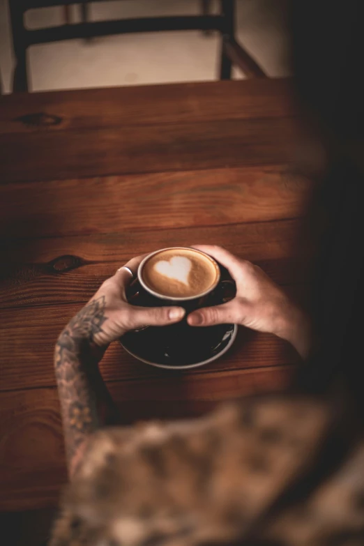 a person with a tattoo sitting at a table and holding up a coffee cup