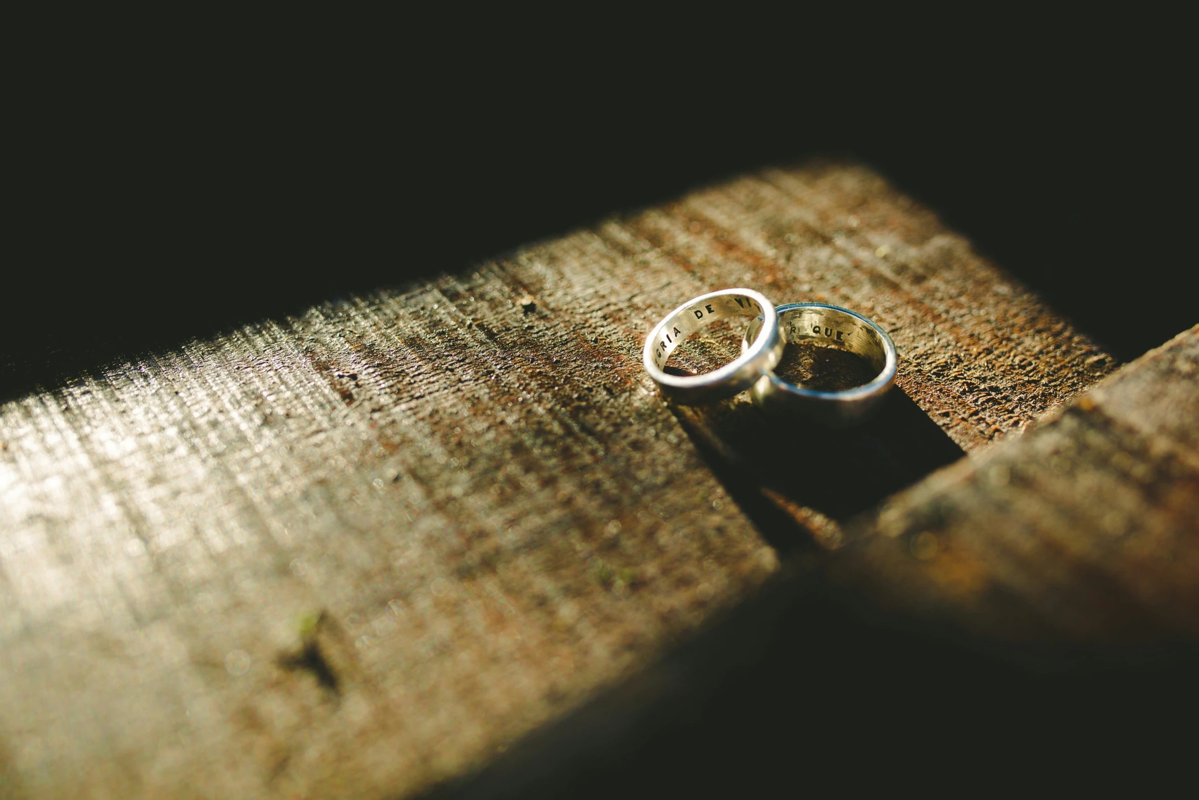 two wedding rings are resting on a piece of wood