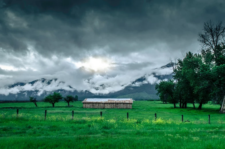 a barn in a field next to trees with mountains in the background