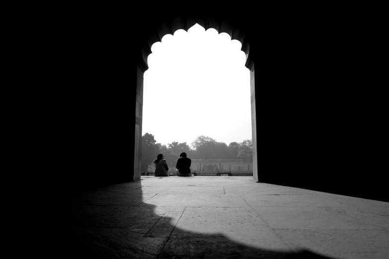 two men sit by an arched window at an old building