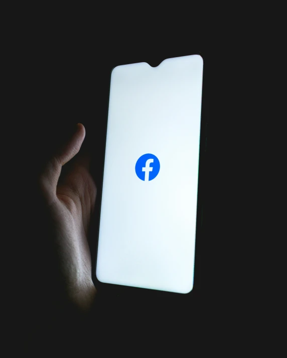 a hand holding an iphone with a facebook logo on it