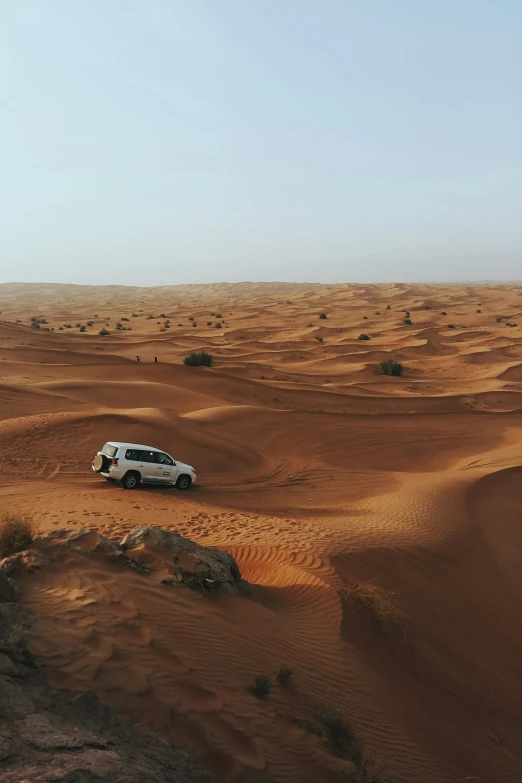 a white car traveling through a desert with sand