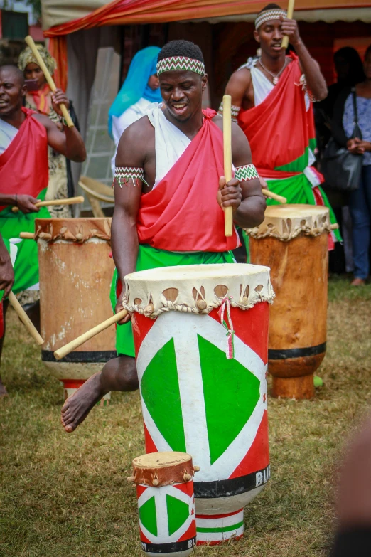 man in ethnic costumes playing instruments with other drummers